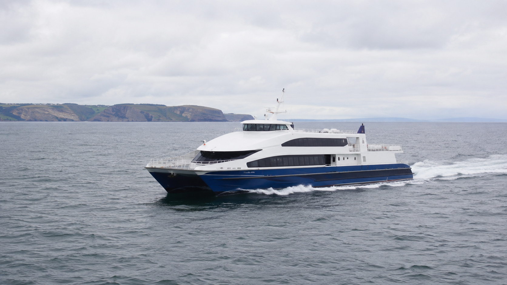 Passenger ferry crossing the Irish Sea near a green coastline